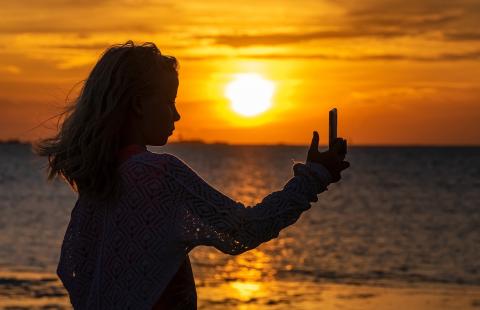 Teenage girl takes selfie at a beach during sunset.