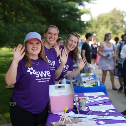 Three students waving at Society of Women Engineers table.