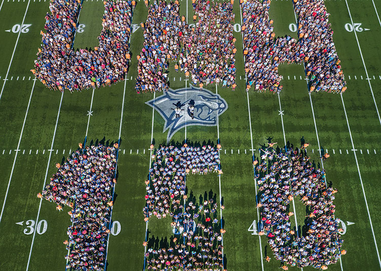 an aerial photo of UNH faculty, staff and students spelling out UNH 150 at Wildcat Stadium 