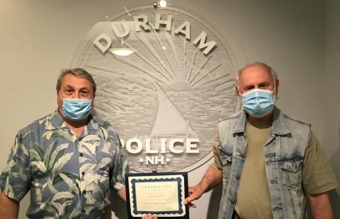 Bob Hylen giving Police Cheif David Kurz a certificate in front of the Durham Police logo