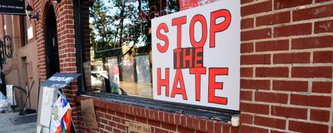 "Stop the Hate" sign in storefront window with flowers in front.