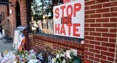 "Stop the Hate" sign in storefront window with flowers in front.