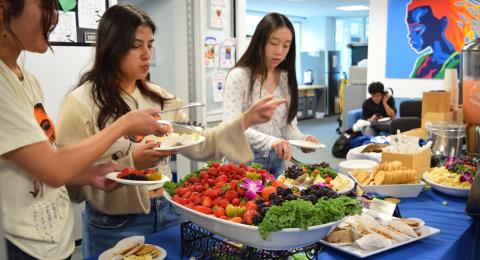Three students in front of some fresh fruit at a Kickoff and Community Gathering event