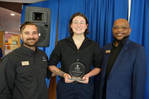 Three people smiling, one holding a trophy