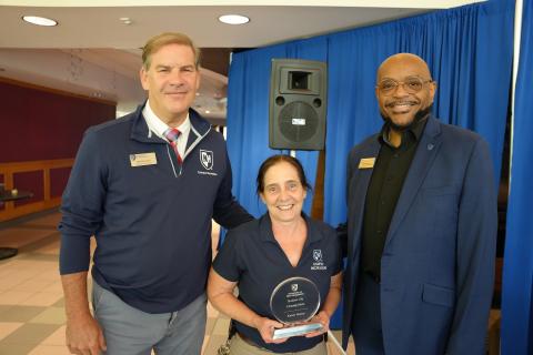 Three people smiling with one holding a trophy