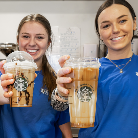 Two student employees at Zeke's Cafe holding Starbucks coffee drinks
