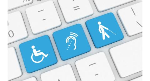 Close up view of a computer keyboard. Three keys are light blue. One has a symbol of a person in a wheelchair. One has a symbol for assistive listening. One has a symbol of a person walking with a cane.