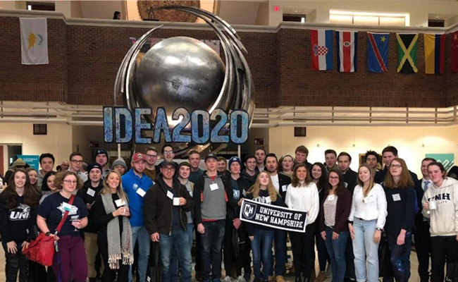 Large group of UNH students holding UNH banner pose at BU Idea Conference