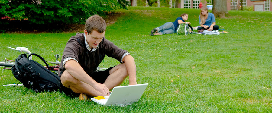student sitting on lawn working on laptop