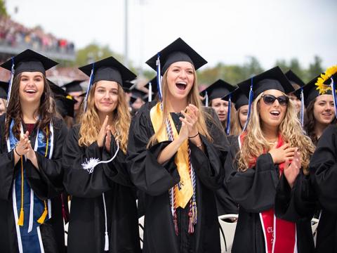 Graduating women in cap and gown clapping