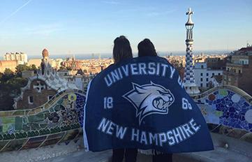 UNH students abroad with UNH flag draped across their backs