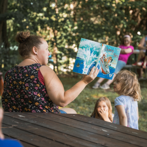 woman reading a picture book to two young girls at a picnic table