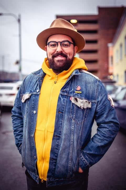 A man in a hat and a yellow sweatshirt with a denim jacket on top