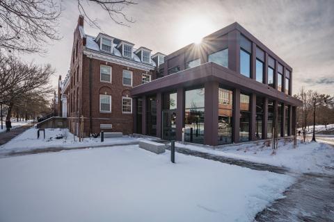A photo of newly remodeled Huddleston Hall in the snow with the sun shining behind it.