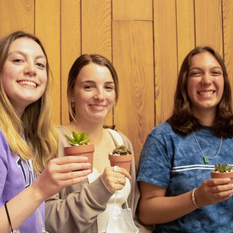 Three students holding small succulents in pots