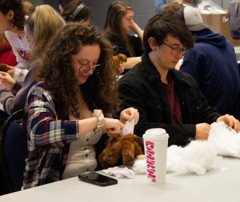Two students putting stuffing in plush moose.