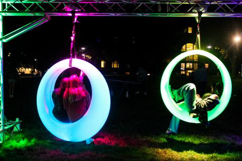 Students sitting inside circular glow swings at night.