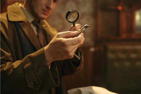 Man holding magnifying glass up to tweezers holding small rock.