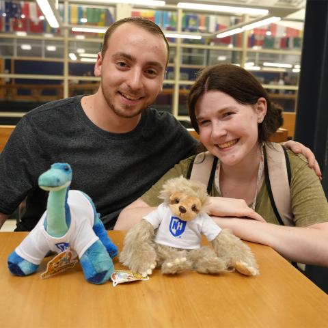 Two students with stuffed dinosaur and stuffed sloth.