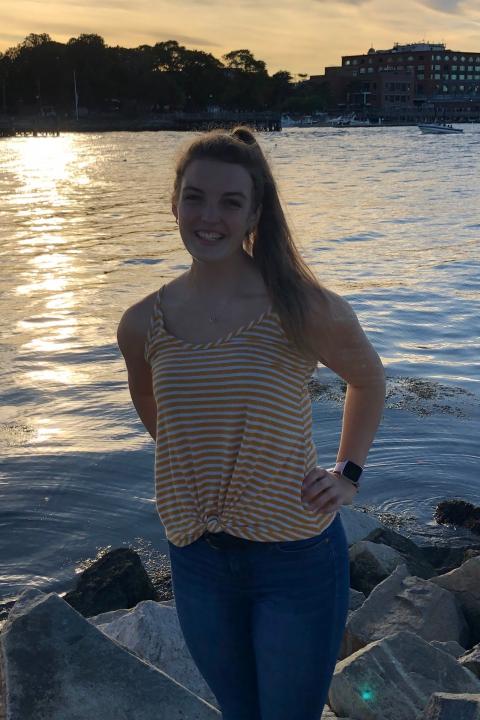 Young woman in yellow striped shirt smiles on the beach.