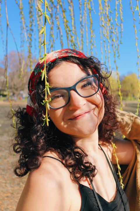 Young woman wearing glasses and a head scarf, posing underneath a tree