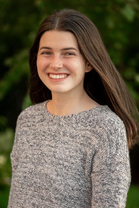 Young woman in a grey sweater smiling outdoors