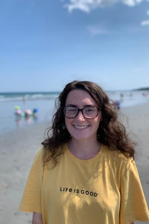 Brunette woman wearing glasses and a yellow t-shirt standing on the beach