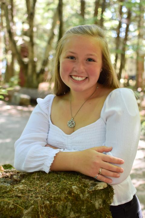 Young blonde woman in a white shirt leaning on a rock in the woods.