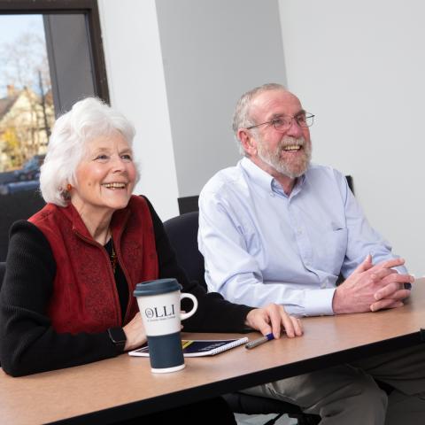 Two people with white and grey hair sitting in an academic conference room