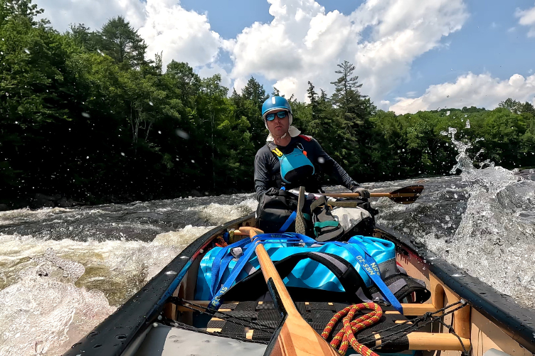 A man in a blue helmet canoes through some rapids