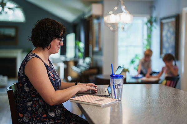 Woman on laptop in her kitchen and kids in the background 