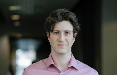 Male researcher wearing pink shirt stands in a hallway