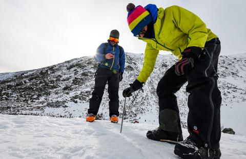 Two researchers in winter gear stand on a snowy mountain