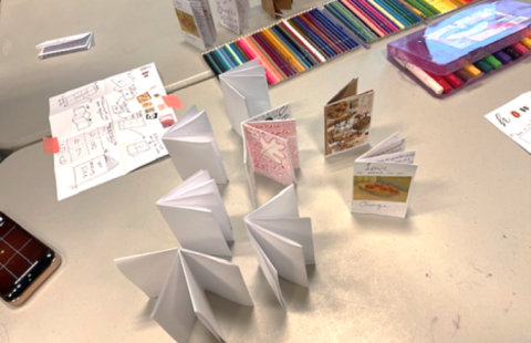 photo shows art supplies on table and done and in progress zines standing up