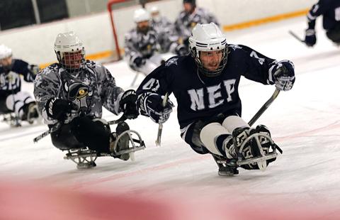 Two sled hockey players skate up the ice