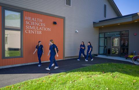 Students in blue scrubs walk alongside the Health Sciences Simulation Center