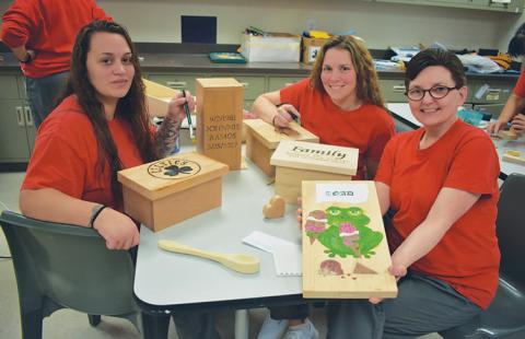 three women in classroom showing their woodworking projects