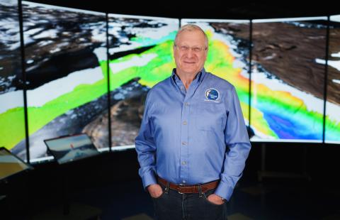 Man in blue shirt stands in front of a screen with mapping graphics on it