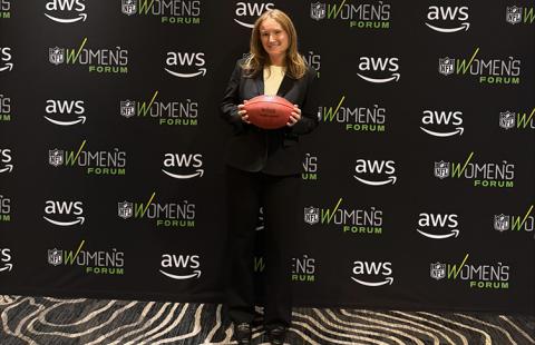 A woman in a black suit holds a football in front of her in front of a black backdrop