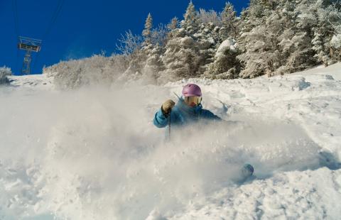 Skier in blue jacket makes a spray of powder