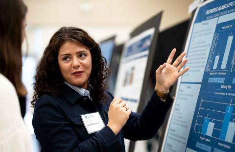 A woman looks back while speaking to a guest as she explains research on a poster in front of her