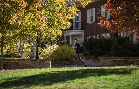 Image of a male UNH student walking on campus surrounded by bright fall foliage