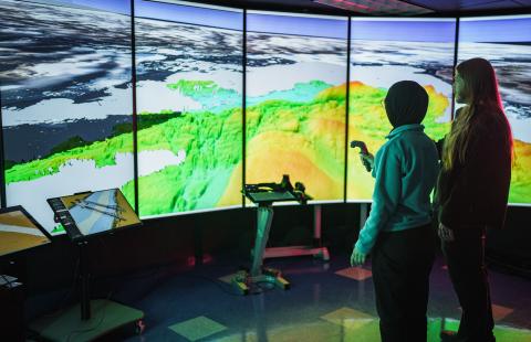 Two people stand in front of the large screen inside UNH's Data Visualization Research Lab at the Center for Coastal & Ocean Mapping