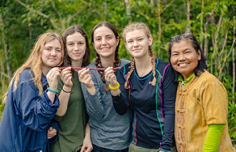 five people standing side by side outside smiling and some are holding a red stick
