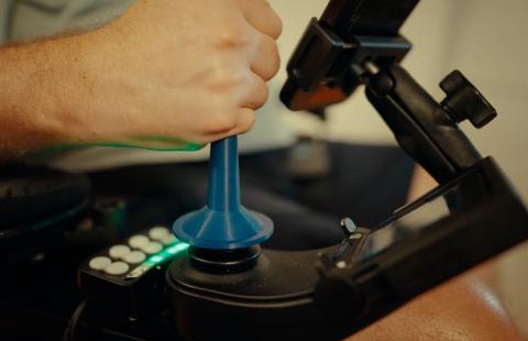 Shane Kulsic uses a 3D joystick adaptation provided by ATinNH to steer his electric wheelchair.”