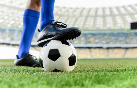 Soccer players holds ball with foot.