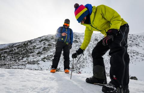 Two people monitor snow in the mountains