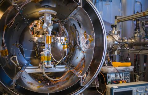 Researcher in blue clean suit looks through a thermal vacuum chamber