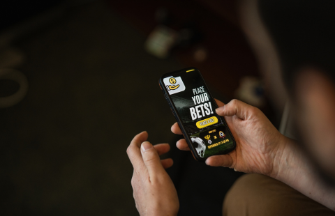 A person holds a smartphone displaying an online sports betting app.