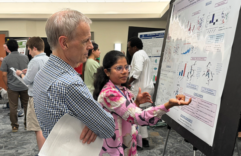 Rick Cote stands next to a student while she describes the work featured in her research poster